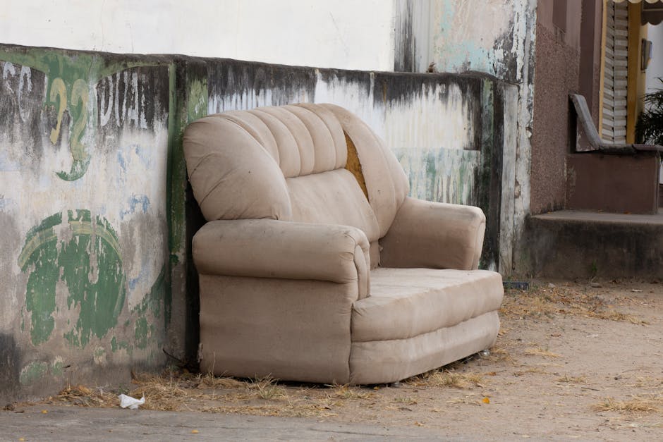 A large pile of discarded furniture and office equipment, including wooden desks, metal-framed chairs with plastic and wooden seats, and small storage units, all in various conditions, with some items